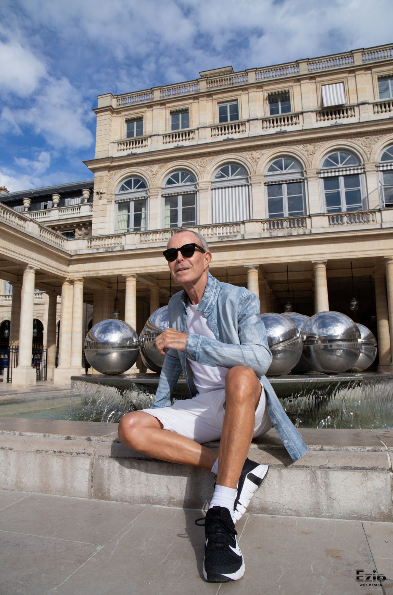 Homme stylé en tenue décontractée assis devant les Boules de Buren au Palais-Royal à Paris.